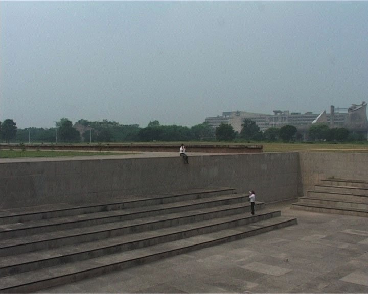 Foto von aus der Ferne aufgenommenen breiten Stufen und einer Steinmauer. Eine Person steht auf den Stufen, die andere Sitz auf der Mauer.
