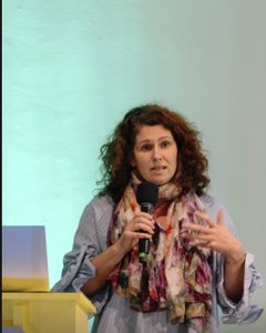 Ein Foto der Projektleiterin Anamarija Batista, die mit einem Mikrofon in der rechten Hand spricht und mit der linken Hand gestikuliert.