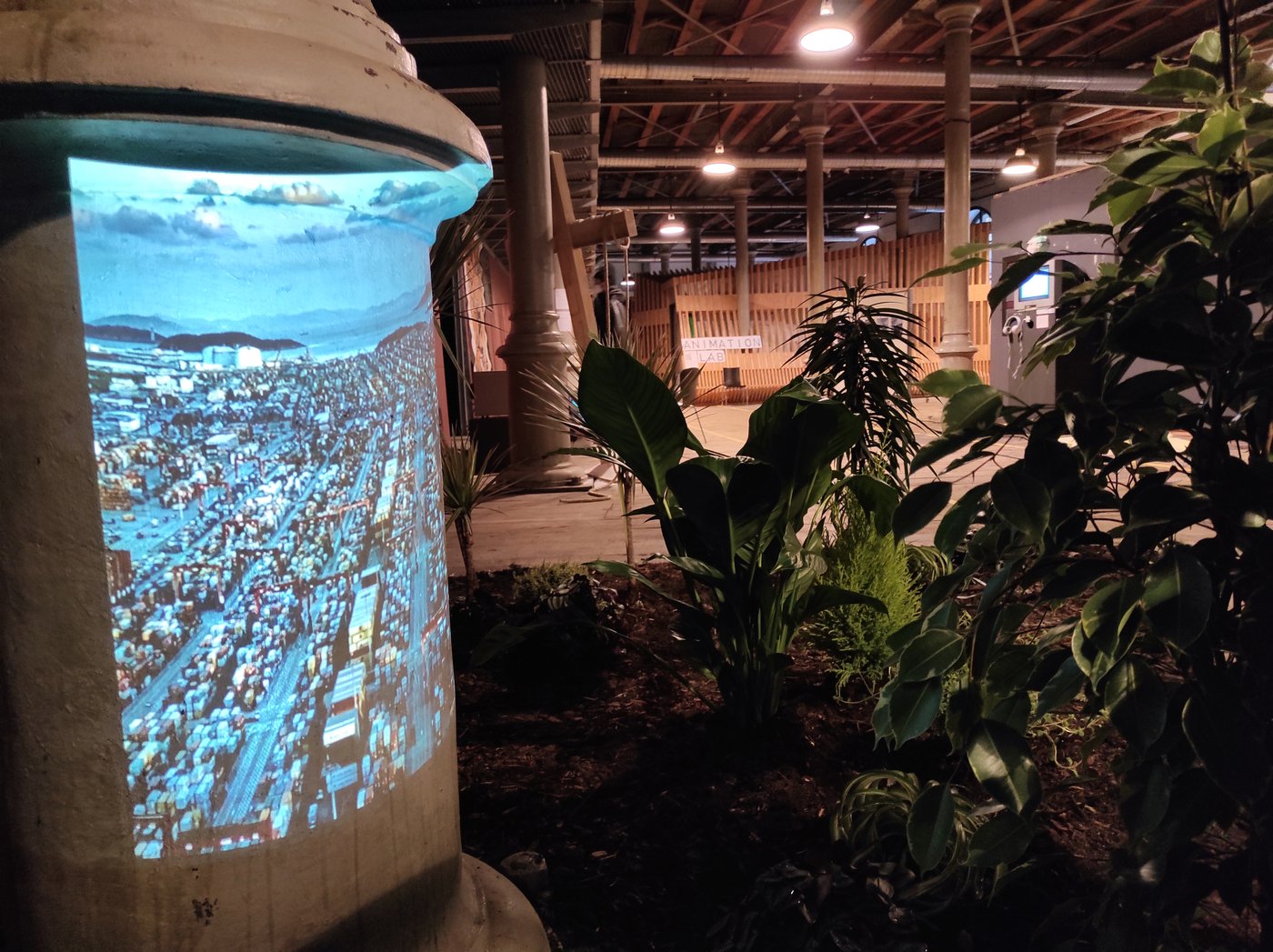 Timotheus Column with projection with container storage space, next to it earth with plants. In the background you can see the wooden fixtures in the studio house.
