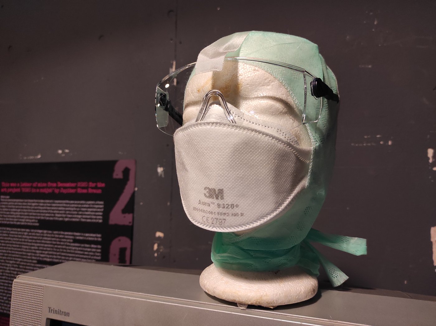 Finn A Styrofoam head with FFP2 mask, goggles and head protection stands on a Triniton monitor.