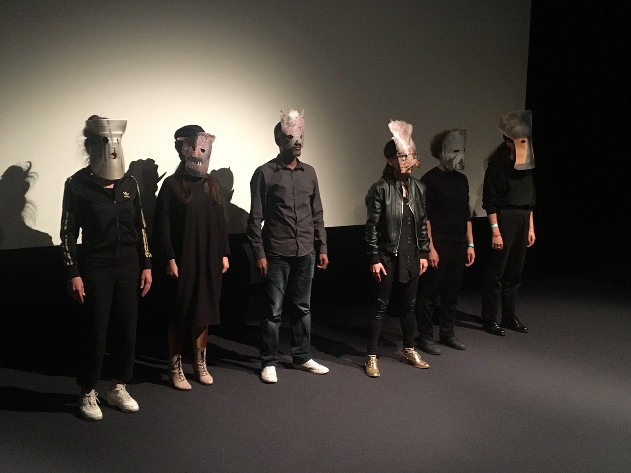 6 people in dark clothes with masks lined up in a row
