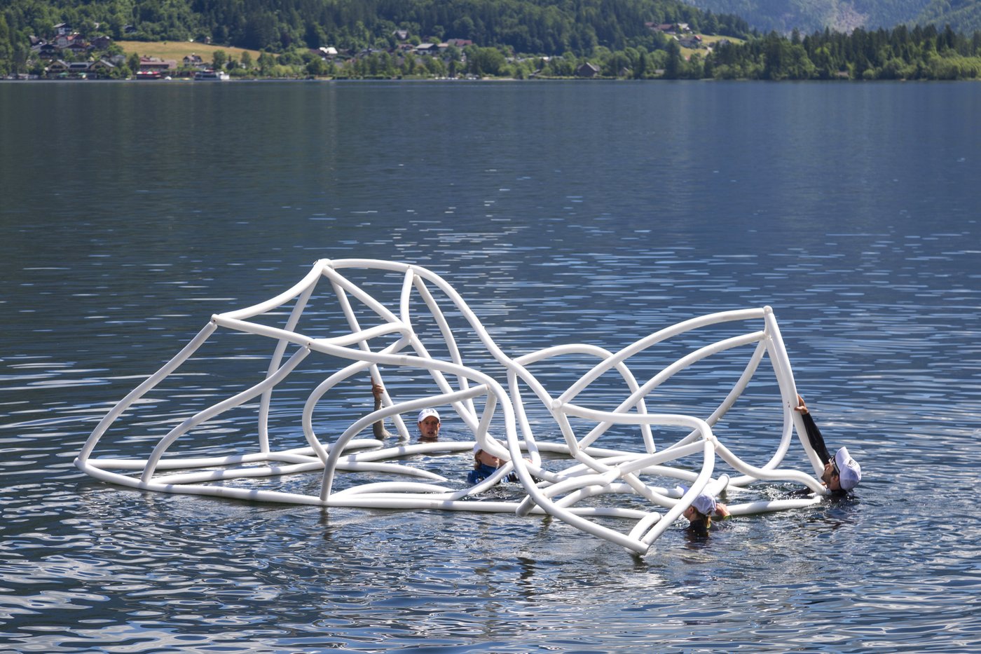 Vier Menschen schwimmen in einem Bergsee mit einem Objekt, das aussieht wie ein großes, weißes biegsames Gerüst