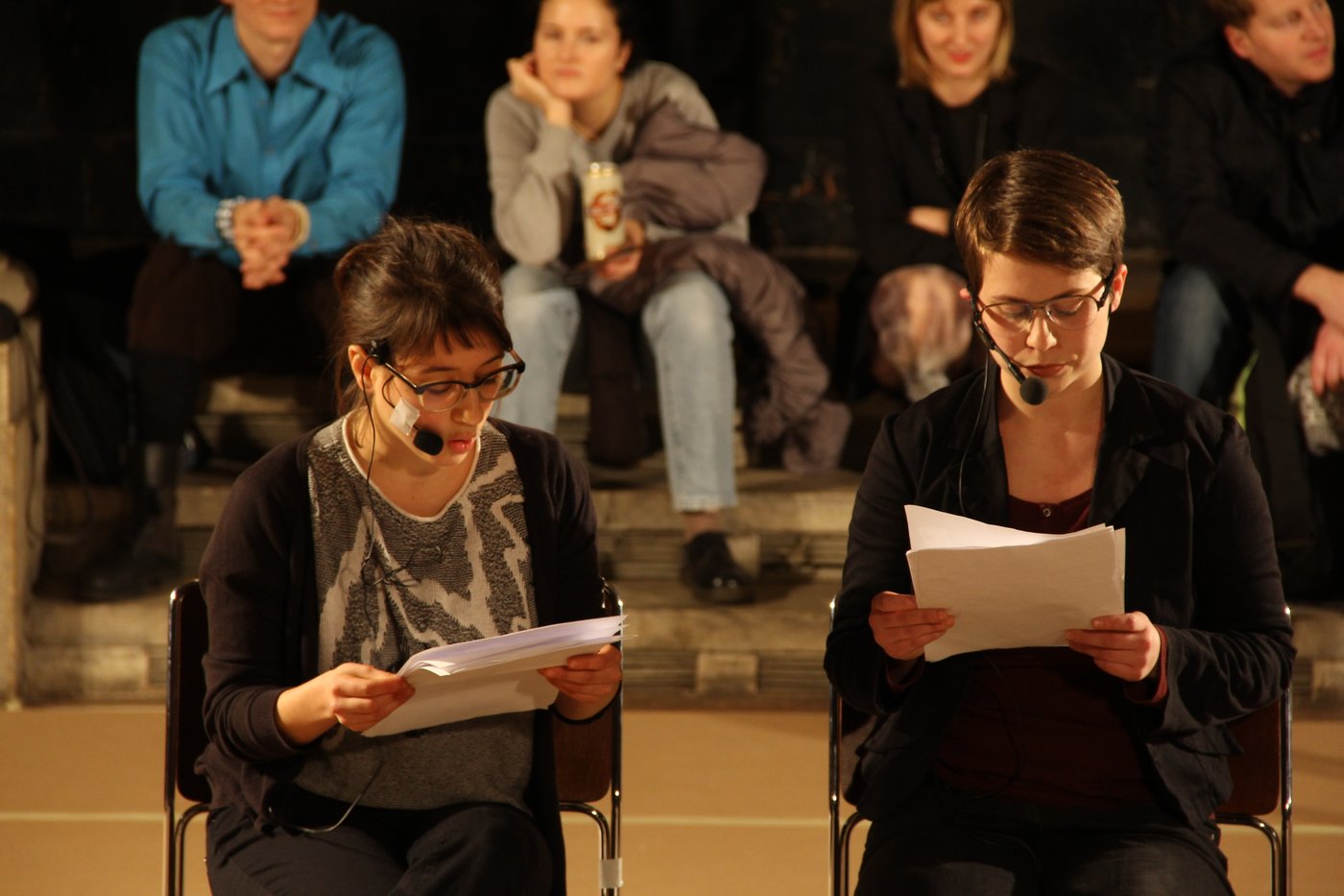 Two performers read from the manuscripts they hold in their hands