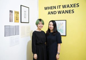 Foto von zwei asiatischen Frauen die vor AUsstellungsstücken stehen und in die Kamera lächeln