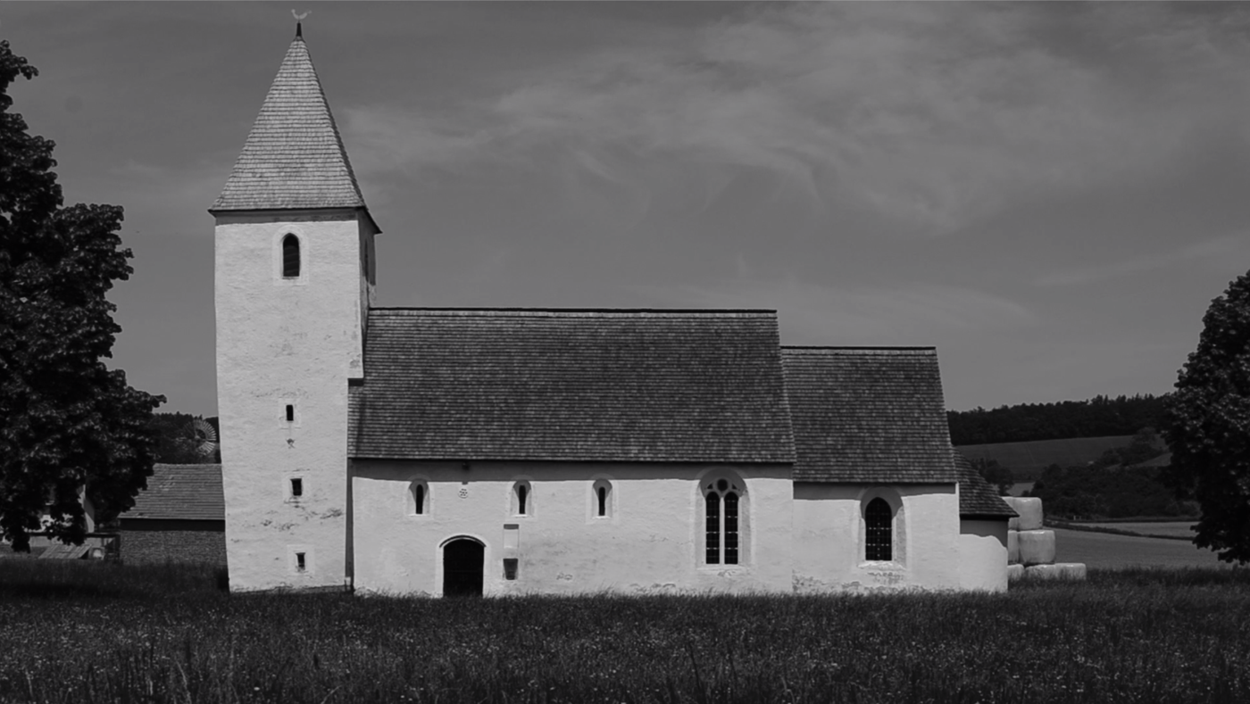 schwarz-weiß Foto einer ländlichen Kirche, rundherum Feld und Wald