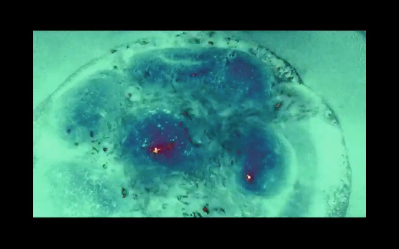 Videostill. Abstrakte Bildkomposition mit invertiert wirkenden Farben, vorrangig Türkis mit Dunkelblauen und Weinroten Akzenten.