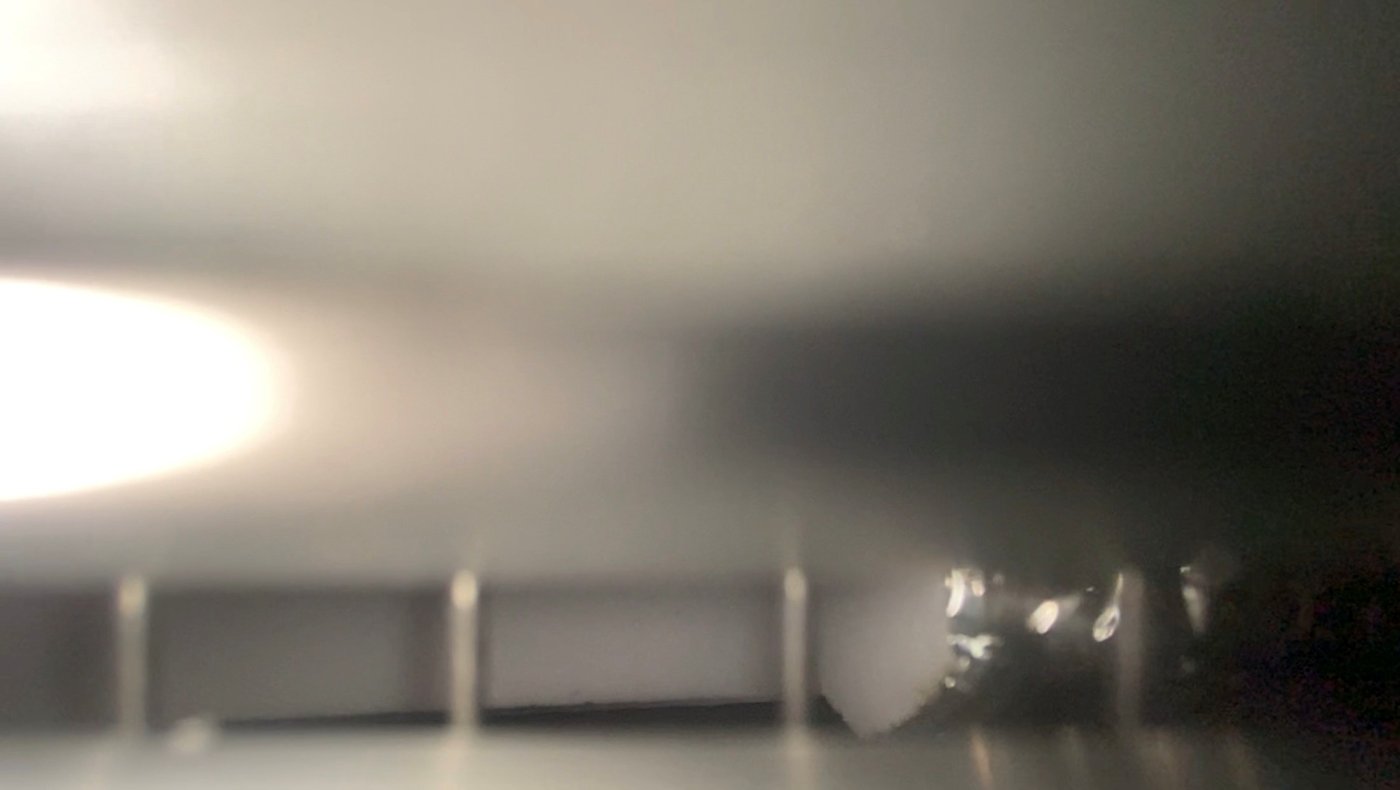 Videostill. Verschwommenes Bild eines metallisch wirkenden Gegenstands, der durch das Bild zur Unkenntlichkeit abstrahiert ist.
