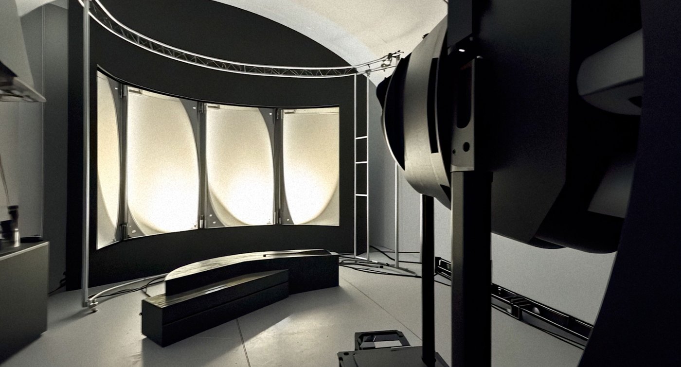 Gewölbter Raum mit einer gebogenen, in vier Segmente geteilten hellen Leinwand, davor eine geschwungene Sitzbank, rechts im Vordergrund ein großer Scheinwerfer.