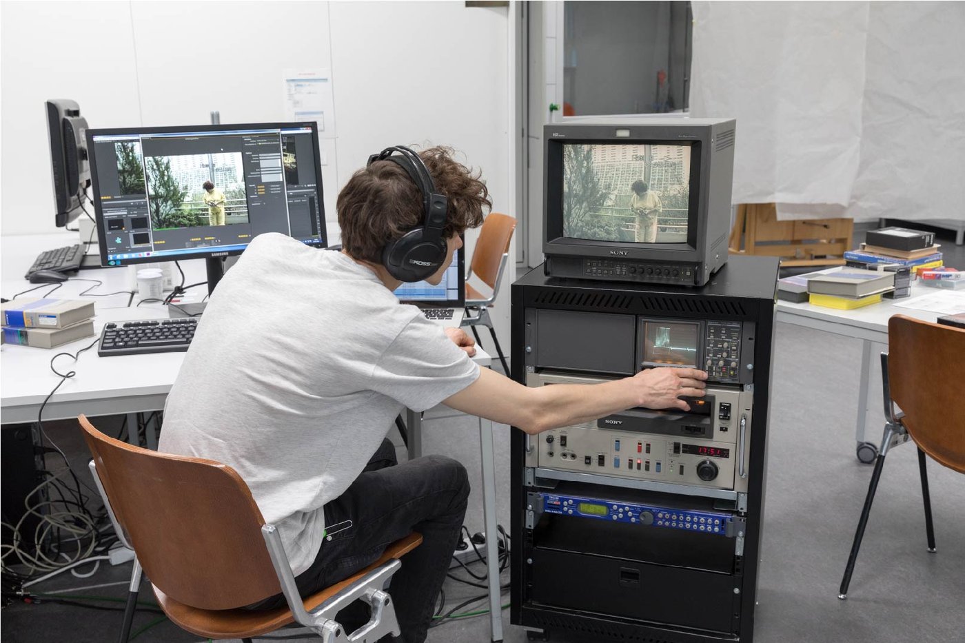 Student with headphones in front of a computer and an old Sony monitor and technical equipment.