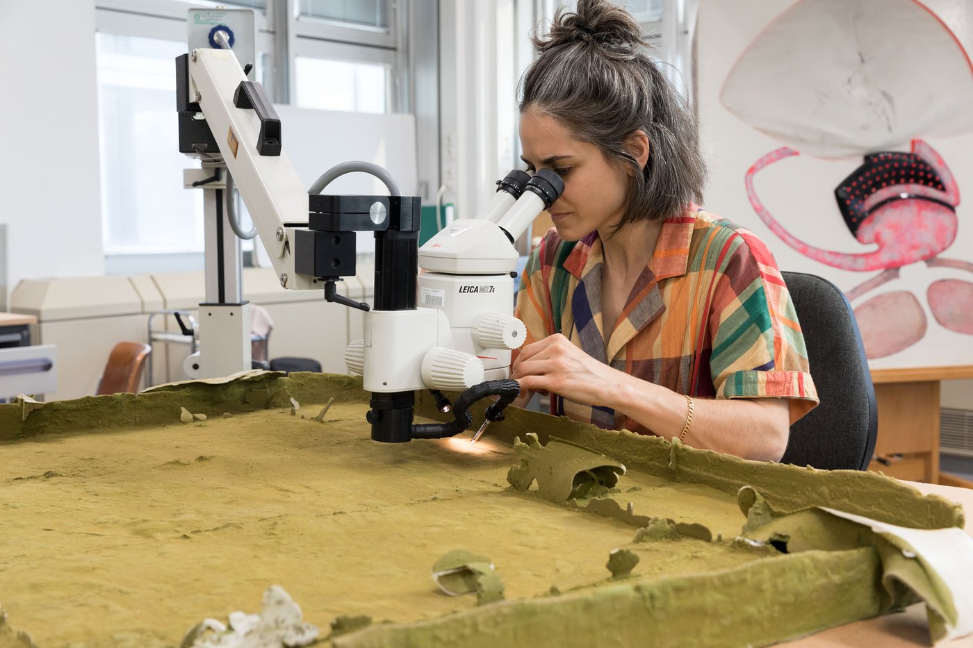 Student with swiveling microscope examining a brown surface.