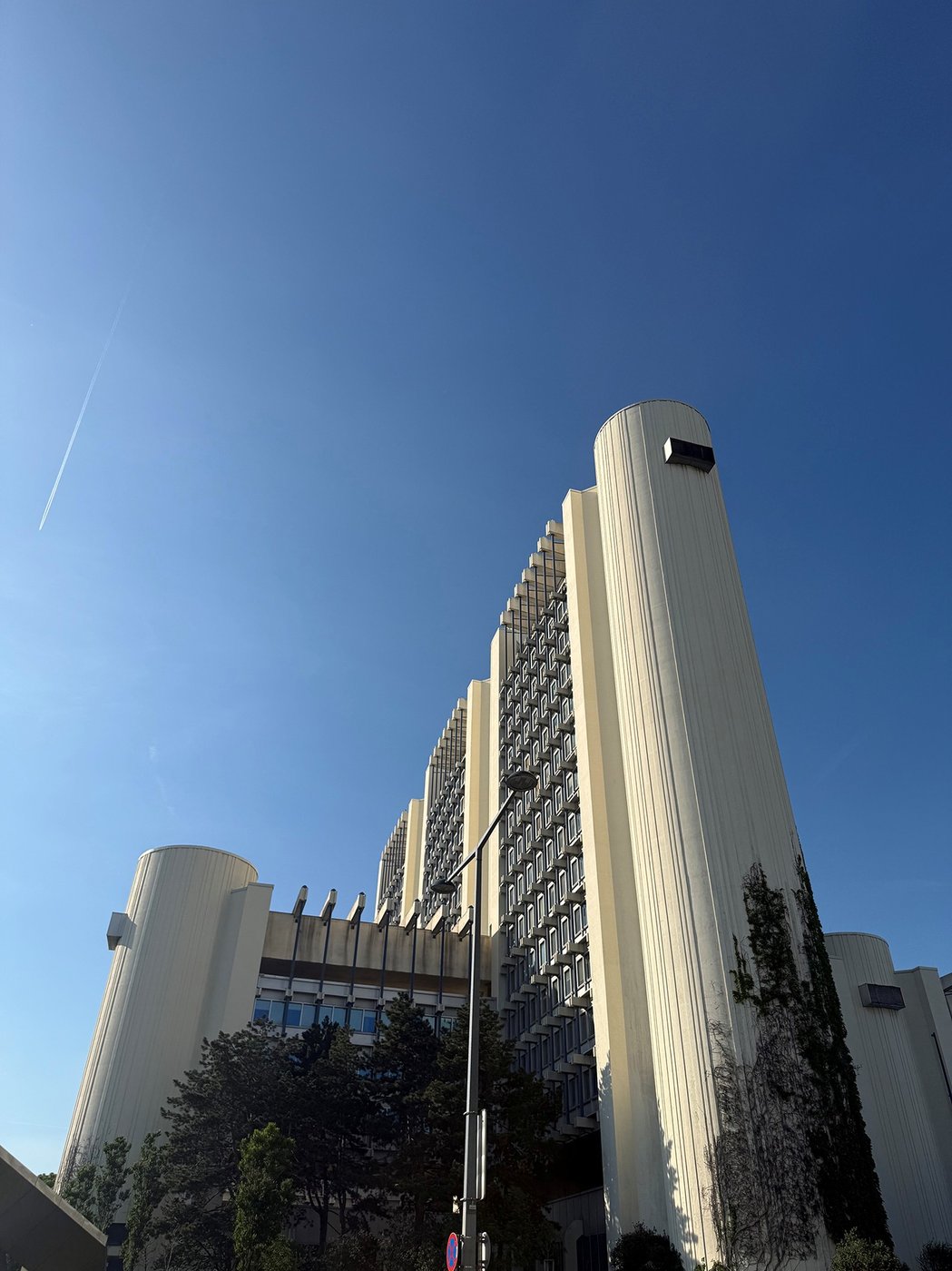 Farbfoto eines in den 1970er Jahren erbauten Gebäudes mit blauem Himmel und weißer Fassade, aufgenommen aus einer extremen Perspektive von unten.