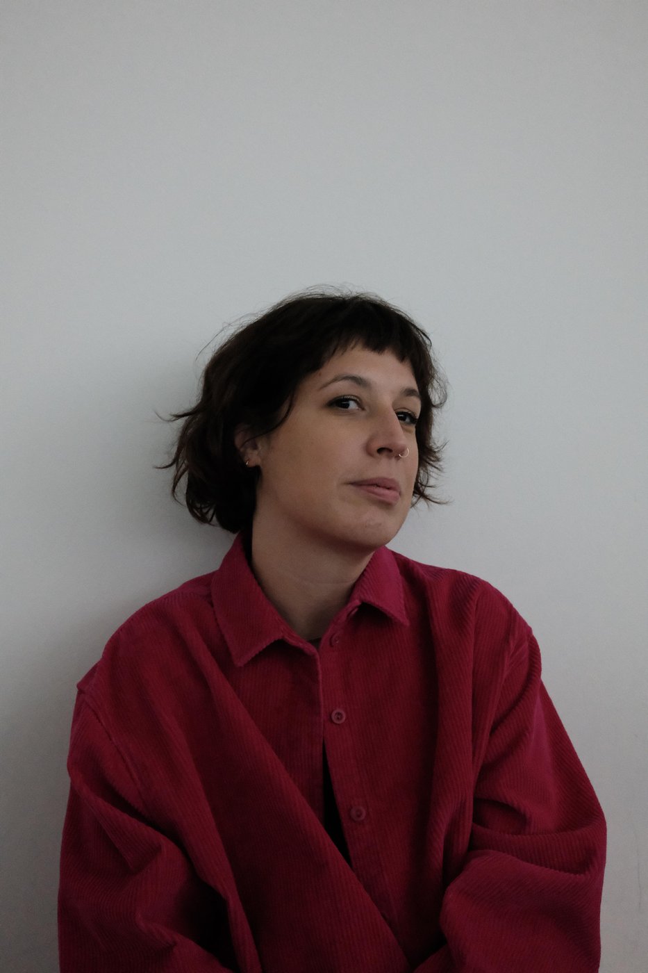 Person mit braunen Haaren und roter Jacke vor weißer Wand