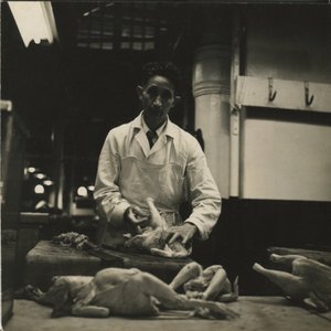 A black-white picture of a butcher with animals in front