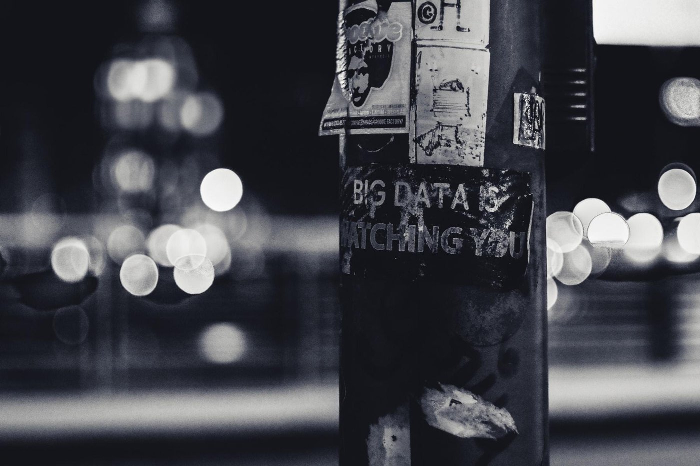 Schwarz-weiß-Foto auf der eine mit Zetteln beklebte Säule zu sehen ist und die Aufschrift "Big data is watching you".