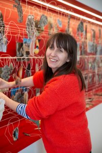 Foto einer lächelnden Frau mit rotem Pulli, die gerade Fotos auf eine Schnur aufhängt