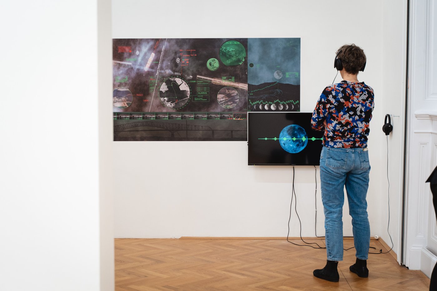 A person with headphones standing in front of an artwork and a screen