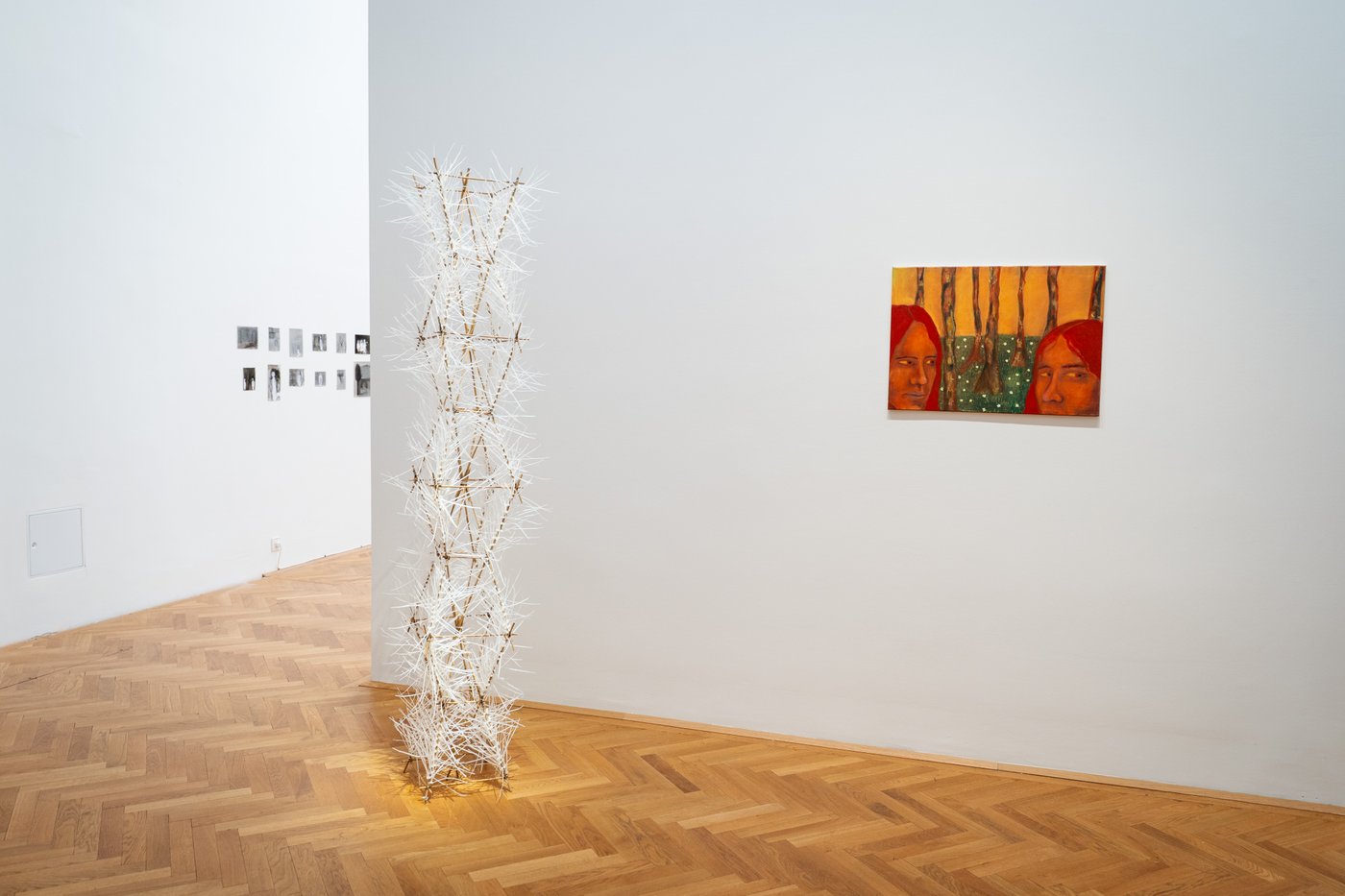 white exhibition objekt and a painting with faces on the wall