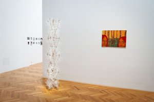 white exhibition objekt and a painting with faces on the wall