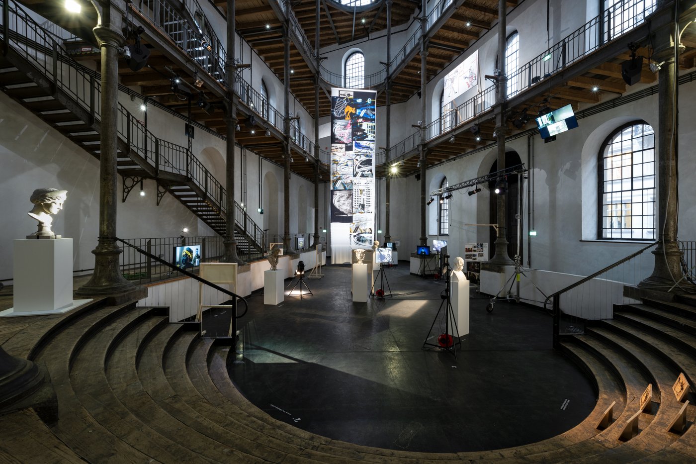 Hoher Raum mit Galerien, auf der untersten Ebene Podeste mit Büsten und dazwischen Hängen Bildschirme