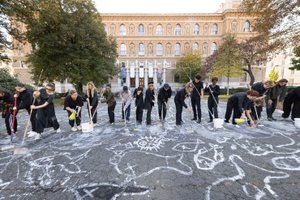 mehrere Studierende die gemeinsam eine Kreidezeichnung mit weißer Farbe und Besen auf den Schillerplatz malen