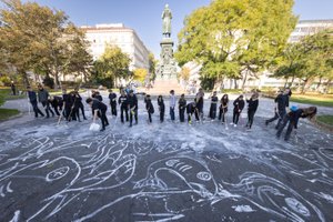 mehrere Studierende die gemeinsam eine Kreidezeichnung mit weißer Farbe und Besen auf den Schillerplatz malen