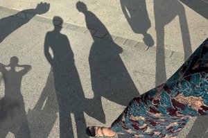 Foto auf dem ein Betonboden zu sehen ist auf dem verschiedene Körperschatten von Personen sind, in der rechten Ecke sind Beine von den Personen zu sehen, die die Schatten auf den Boden werfen
