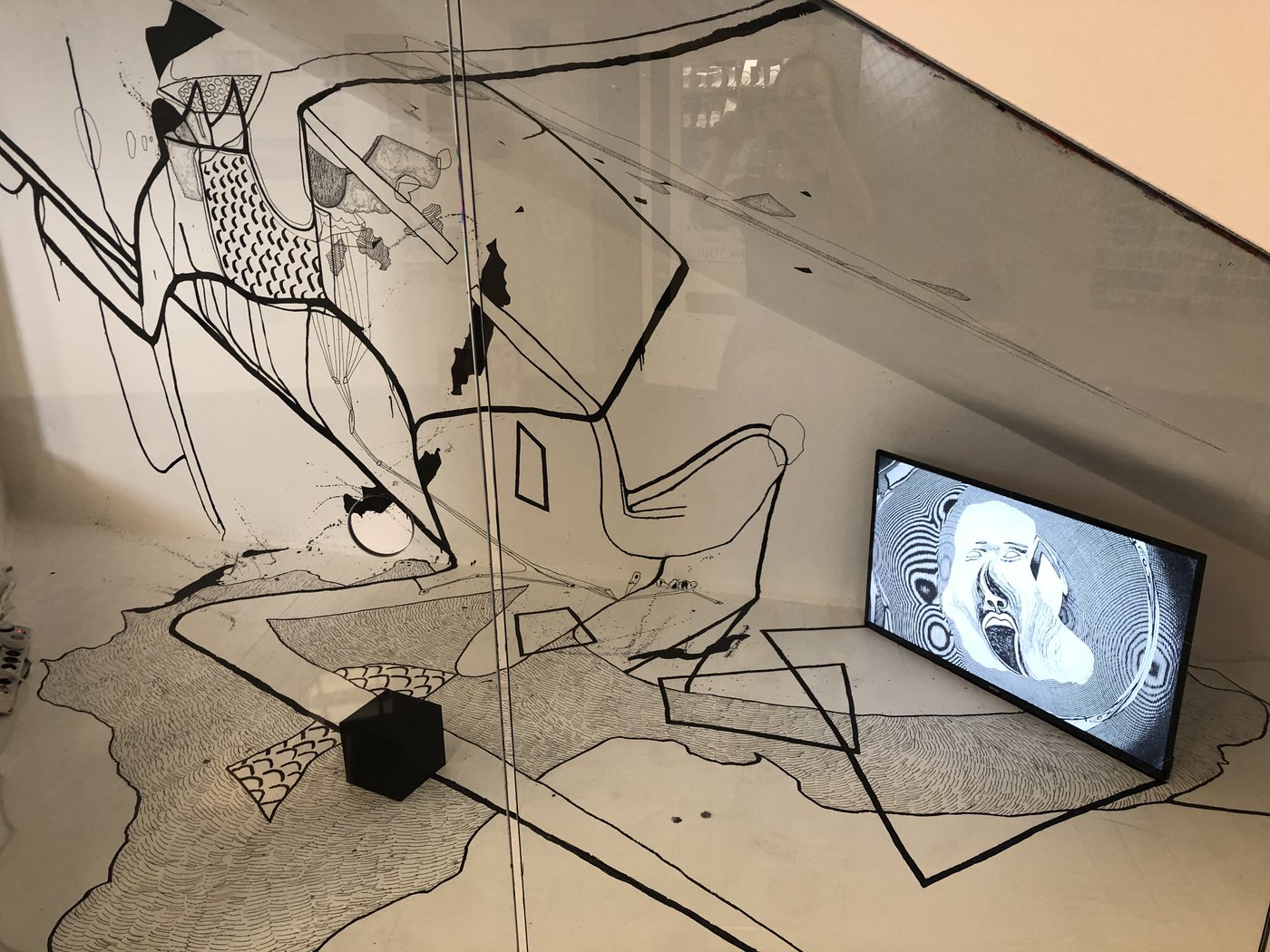 Installationsansicht: Wand mit schwarzem Mustern, in der rechten Ecke steht ein Bildschirm mit gezeichneter Figur