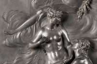Ein silbernes Relief einer nackten Frau die mit ihrer rechten Hand ihre Brust verdeckt und hinunterblickt zu einem Mann der an ihren Füßen kniet und sie umarmt.