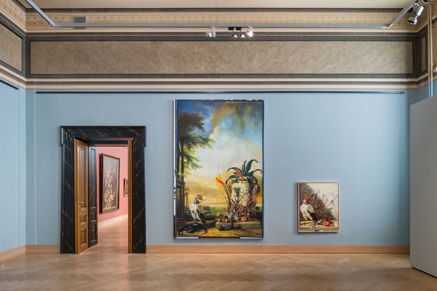 ein blau ausgemalter Ausstellungsraum mit einer grossen schweren alten verzierten Holztür links und zwei grossen Ölgemälden mit Königsgeier