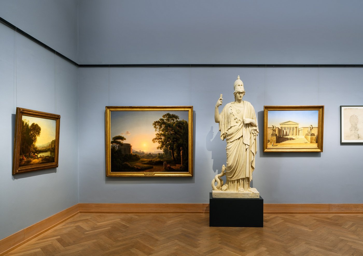 ein blau ausgemalter Ausstellungsraum  mit einer Skulptur und Fotografien sowie Malerei an der Wand