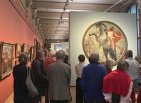 Eine Gruppe von Menschen bei einer Ausstellungsführung in einem Raum mit vielen Gemälden
