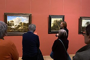 Menschen in einem Ausstellungsraum bei einer Führung mit drei Gemälden auf einer roten Wand