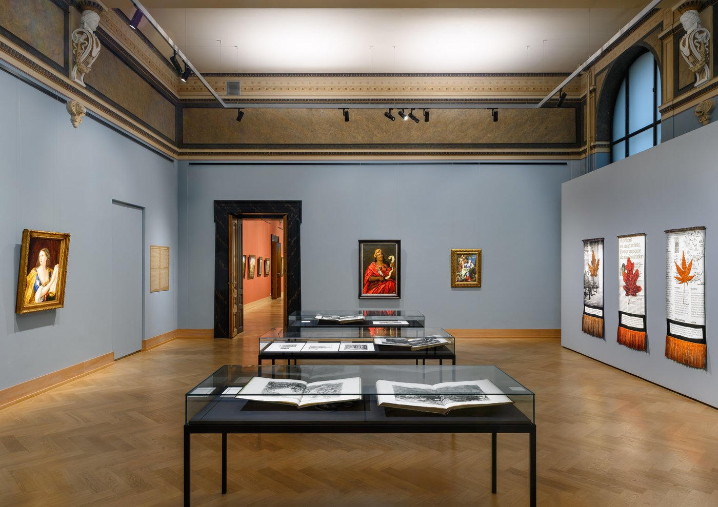 ein Ausstellungsraum mit Gemälden und Glasvitrinen
