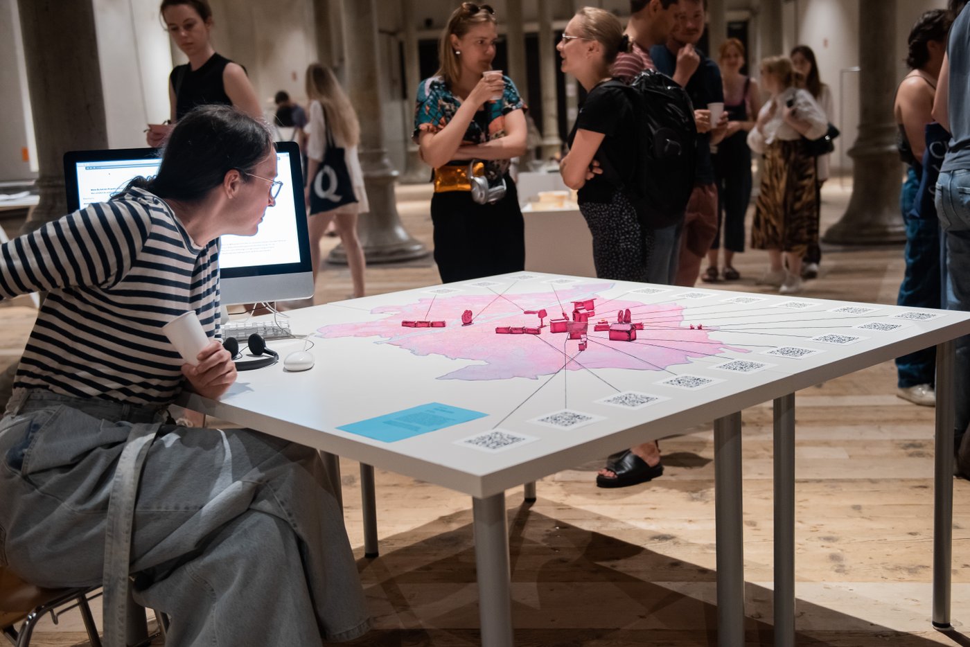 eine Frau sitzt an einem Tisch und blickt auf einen pinken Stadtplan der mit Blöcken Punkte gekennzeichnet hat