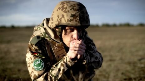 Foto eines jungen Armesoldaten in Uniform der sich die Hände an seinen Mund hält um sie zu wärmen