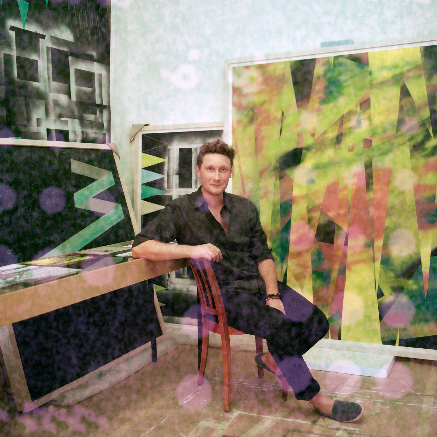 Mann in schwarzer Kleidung sitzt auf einem Stuhl in der Mitte von lebensgroßen Kunstwerken