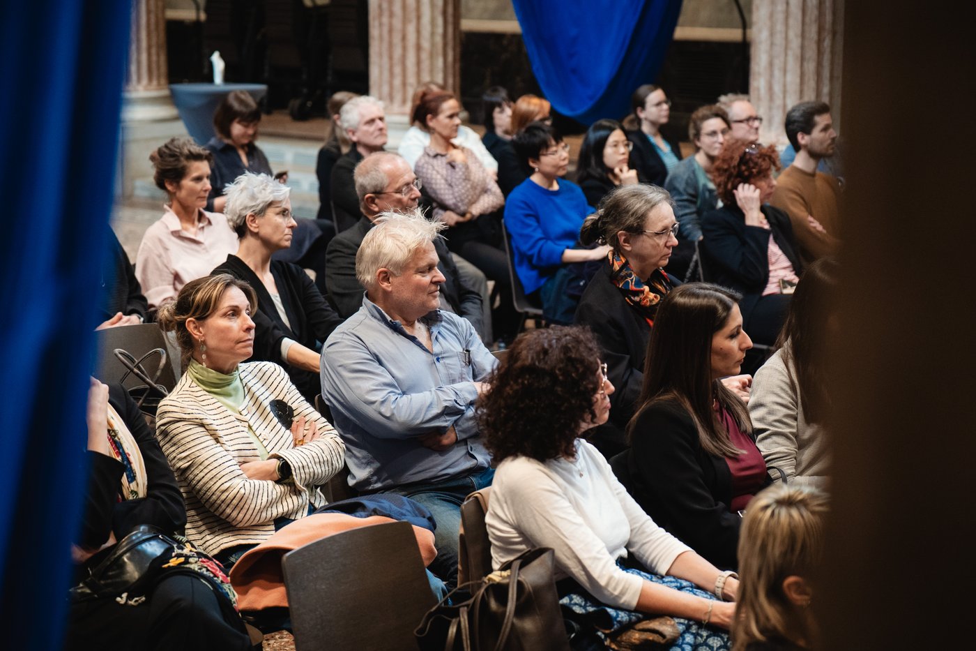 Blick ins  Publikum. Perosnen sitzen in Reihen auf Stühlen und hören dem Vortragenden zu.