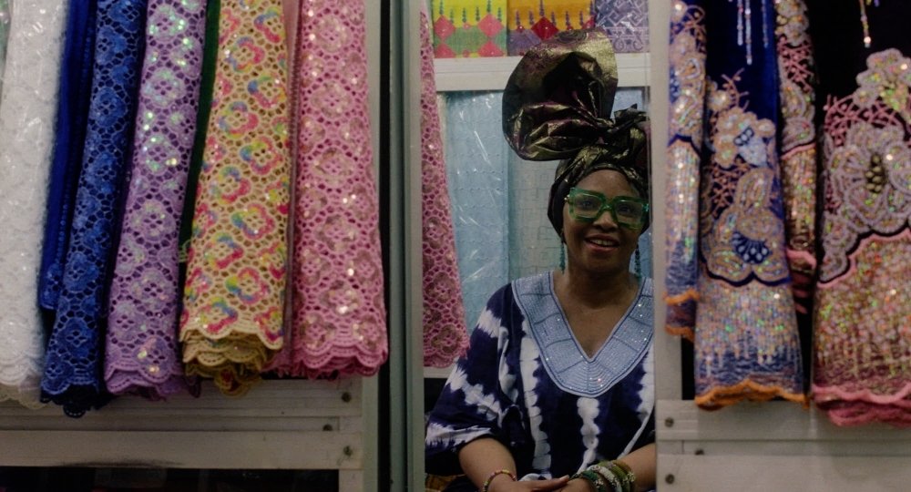 Eine lächelnde Frau sitzt in Laden umgeben von bunten Spitzenstoffen