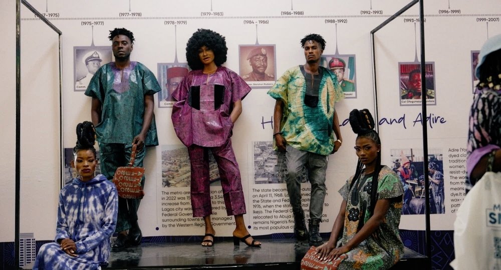 Personen posieren vor einer Werbewand in bunter afrikanischer Spitzenkleidung