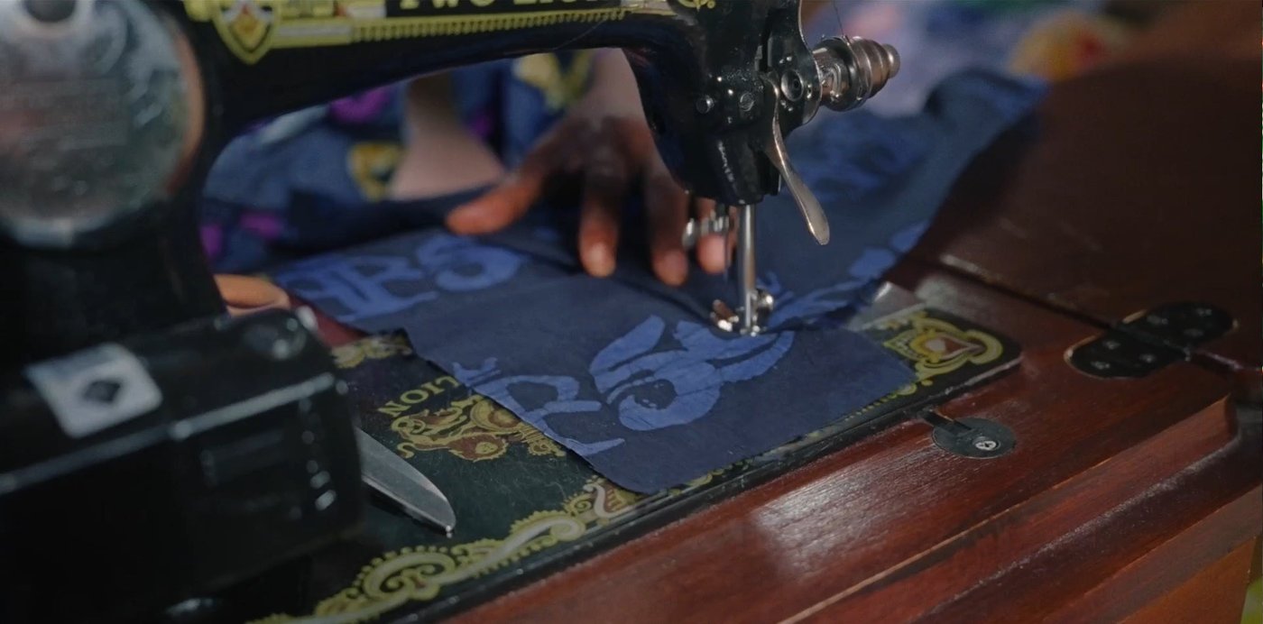 Ein Hand hält einen blauen Stoff an einer Nähmaschine