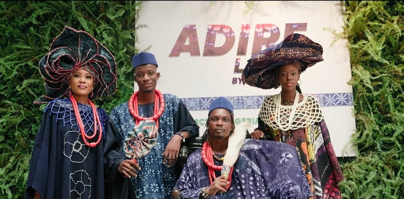 Vier Personen in eleganter Spitzenkleidung im afrikanischen Stil stehen vor einer Werbewand