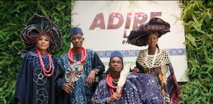 Vier Personen in eleganter Spitzenkleidung im afrikanischen Stil stehen vor einer Werbewand