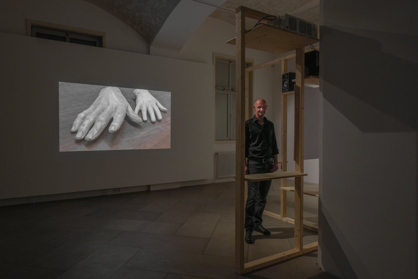 Der Künstler steht vor seiner Videoarbeit auf der man Hande sieht