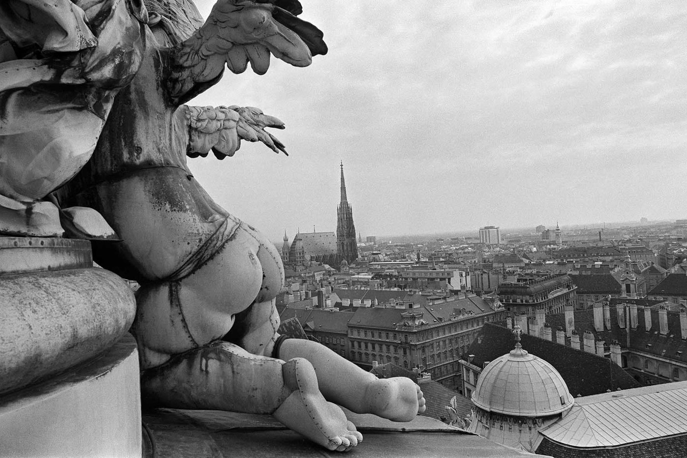 Foto von einem Dach aus, hinteransicht eines Putto mit Flügeln, schwarz-weiß, Blick auf die Dächer der Stadt Wien und den Stephansdom