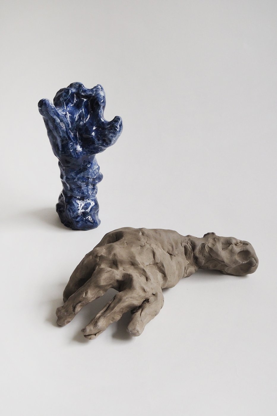 Foto von zwei aus Ton gefertigten Händen, eine liegt mit der Handfläche die andere ist blau glasiert und hat eine aufrechte Handhaltung ohne ausgeformte Finger