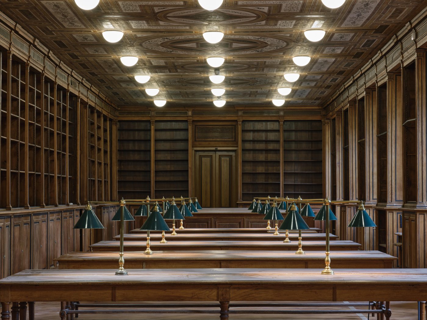 Ansicht einer leeren Bibliothek mit Lesetischen und grünen Tischlampen