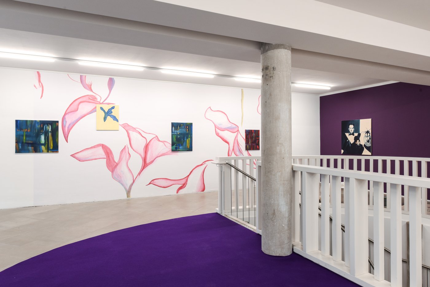 Raum mit Lila Boden und Lila wand rechts, ein Treppenabgang und eine Säule auf der rechten Bildhälfte, im Hintergrund an der Wand sind große rosa Blumen gemalt, dazwischen Gemälde in bunten Farben an der Wand