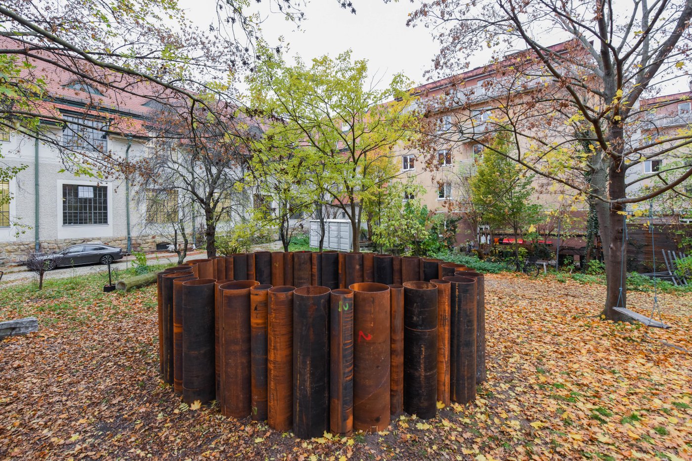 In einem Garten stehen große, verrostete Röhren in einem Kreis angeordnet