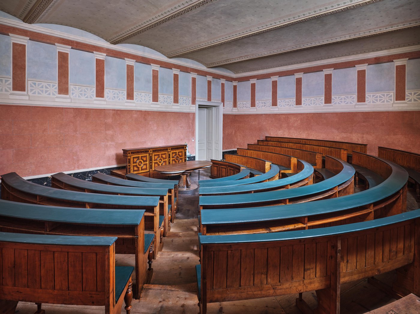 Ansicht eines Vortragssaales mit im halbkreis angeordneten Lehrstühlen und Rednerpult, Terrakottawände