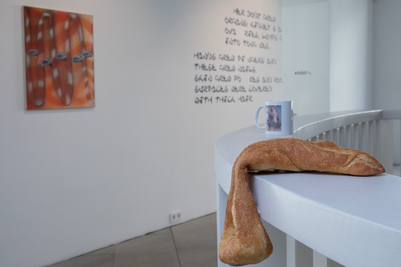 Ein Stück Brot liegt auf einem Geländer, im Hintergrund ist schwarze Schrift auf einer Wand und eine Malerei mit roter Grundfarbe